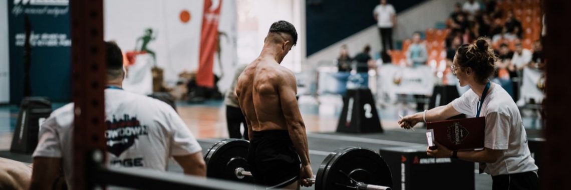 A weightlifting athlete prepares for a lift during a competition with judges observing.