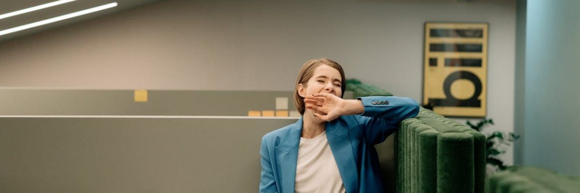 Exhausted woman in blue blazer yawning during workday in corporate office.